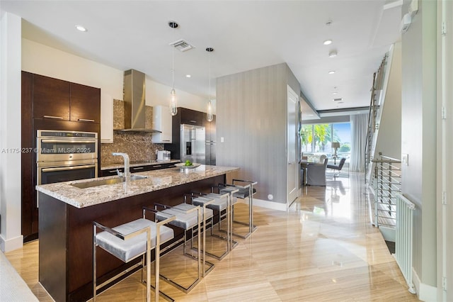 kitchen featuring a breakfast bar area, visible vents, appliances with stainless steel finishes, a sink, and wall chimney range hood