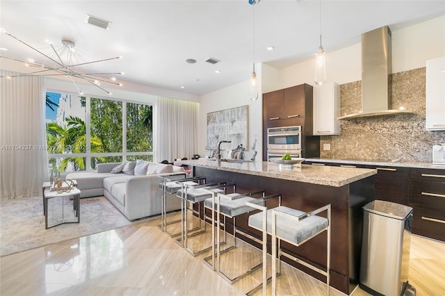 kitchen featuring wall chimney exhaust hood, tasteful backsplash, visible vents, a sink, and a kitchen breakfast bar