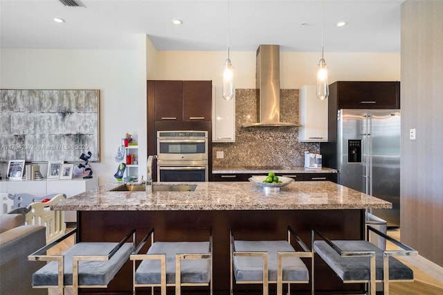 kitchen featuring stainless steel appliances, a breakfast bar, a sink, and wall chimney exhaust hood