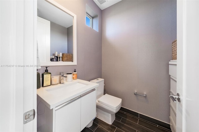 half bath with visible vents, wood finish floors, vanity, and toilet