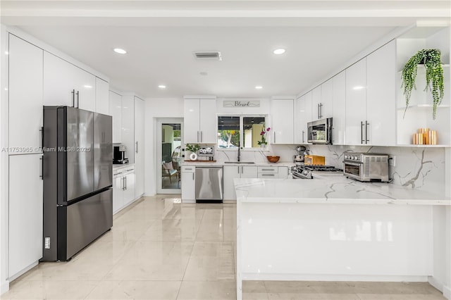kitchen featuring white cabinets, a sink, appliances with stainless steel finishes, a peninsula, and light stone countertops