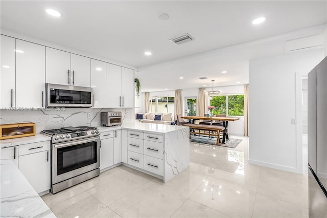 kitchen with visible vents, white cabinets, a peninsula, stainless steel appliances, and decorative backsplash