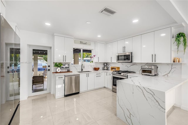 kitchen with modern cabinets, visible vents, light stone counters, a sink, and stainless steel appliances
