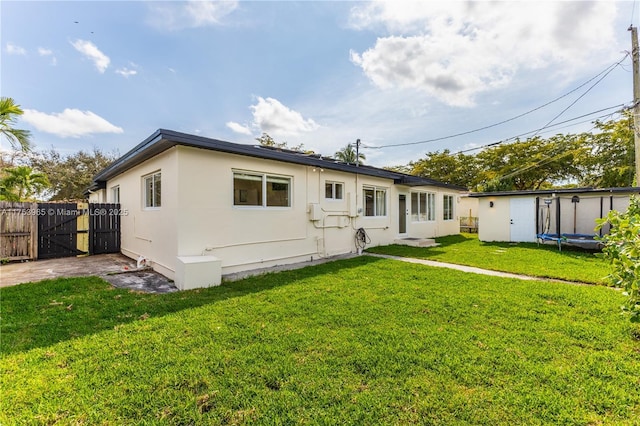 back of house with a trampoline, stucco siding, a gate, fence, and a lawn