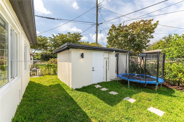 view of yard featuring a trampoline, an outdoor structure, and fence