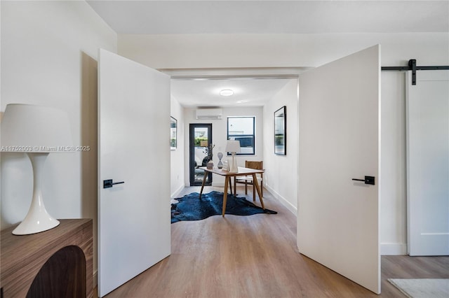 corridor with wood finished floors, a wall unit AC, baseboards, and a barn door