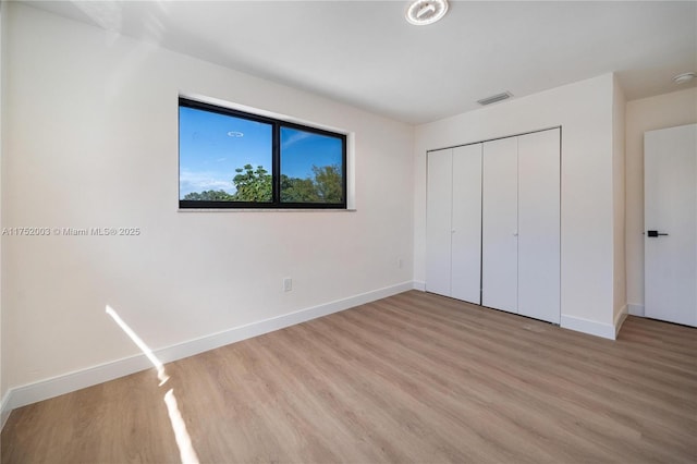 unfurnished bedroom featuring light wood-style flooring, visible vents, baseboards, and a closet