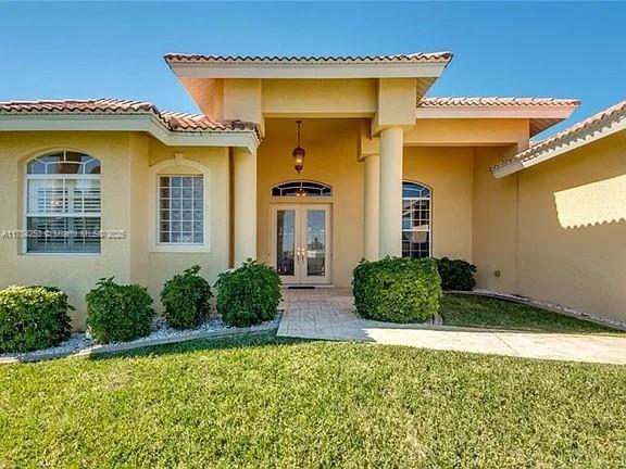 doorway to property featuring french doors, a yard, and stucco siding