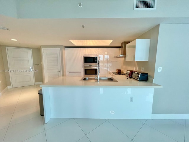 kitchen with visible vents, wall chimney range hood, a peninsula, light countertops, and built in appliances