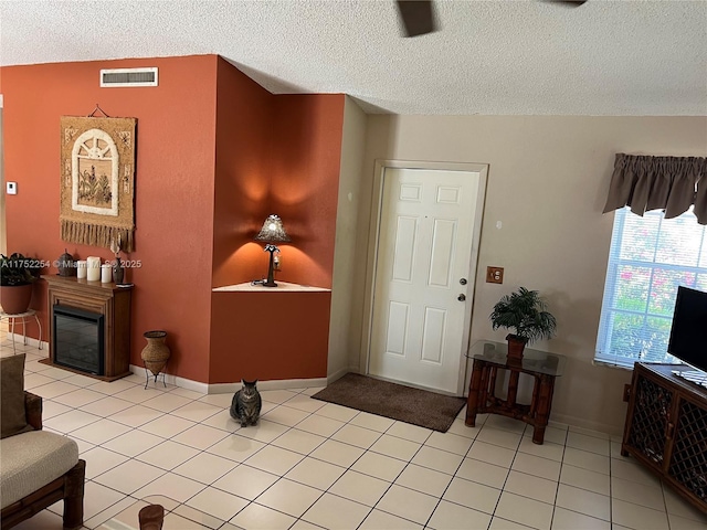 entrance foyer featuring light tile patterned floors, visible vents, a textured ceiling, and a glass covered fireplace