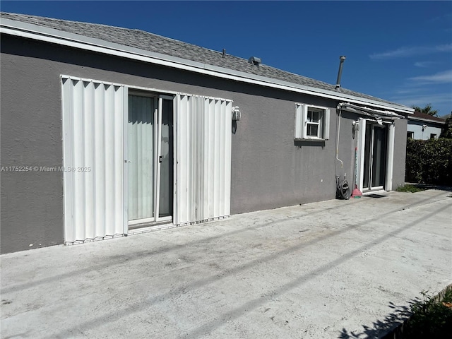 rear view of property with roof with shingles and stucco siding