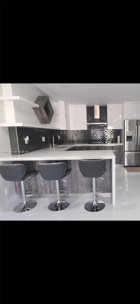 bar with a sink, wall chimney exhaust hood, tasteful backsplash, and stainless steel fridge