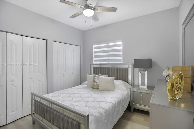 bedroom with light wood-style floors, ceiling fan, and two closets