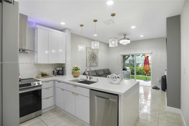 kitchen with a peninsula, a sink, light countertops, appliances with stainless steel finishes, and wall chimney exhaust hood