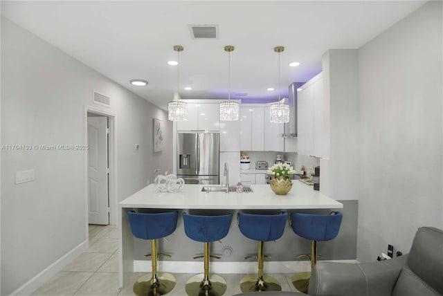 kitchen with stainless steel fridge, visible vents, a peninsula, white cabinetry, and a sink