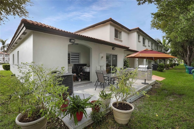 back of house featuring a yard, a patio, stucco siding, central AC, and a tiled roof