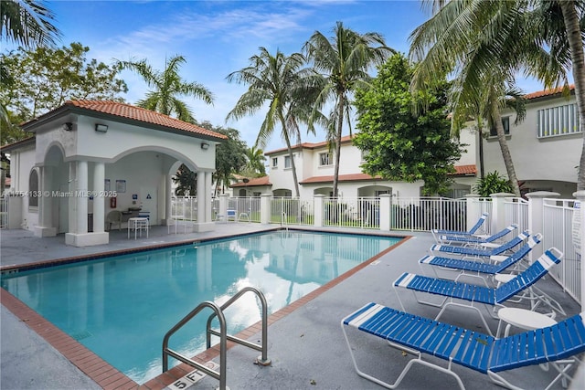 community pool featuring fence, an outdoor structure, and a patio