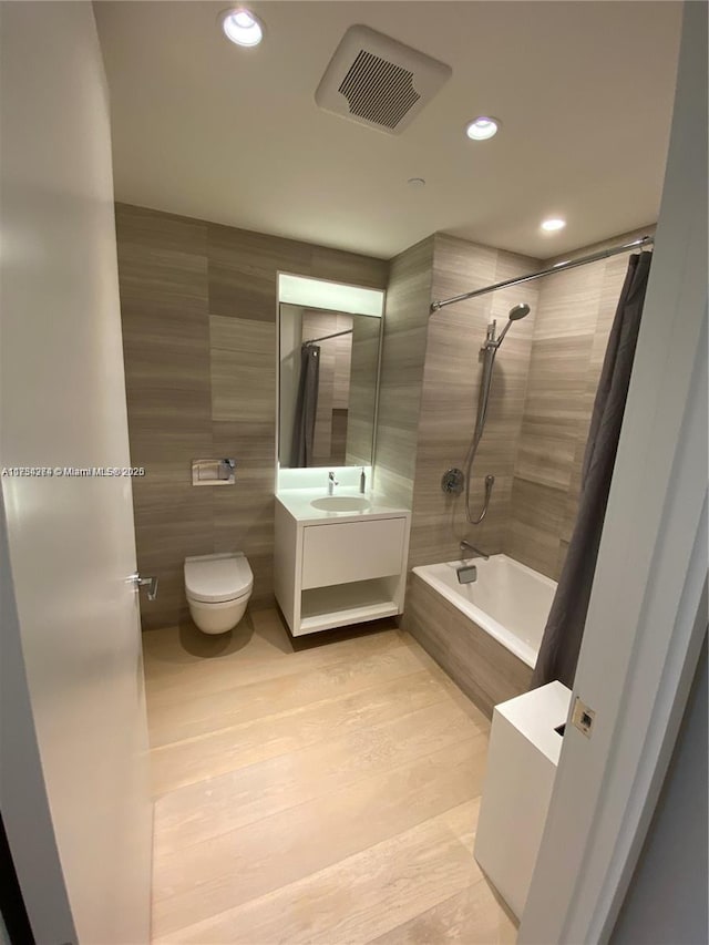 full bath featuring visible vents, toilet, tiled shower / bath, vanity, and tile walls