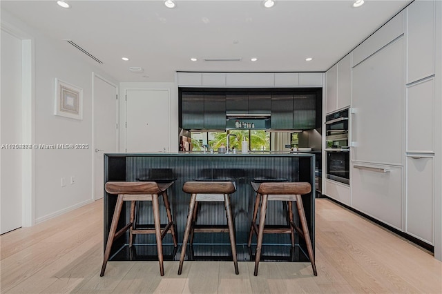 kitchen with recessed lighting, white cabinets, light wood finished floors, modern cabinets, and a kitchen bar