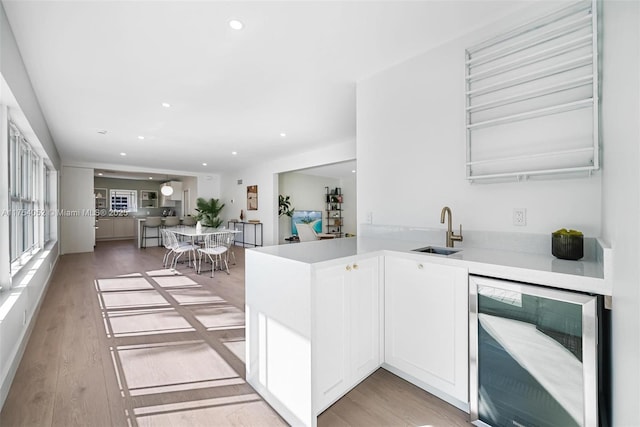 kitchen with light countertops, white cabinets, light wood finished floors, a sink, and beverage cooler