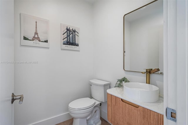 half bathroom featuring toilet, vanity, and baseboards