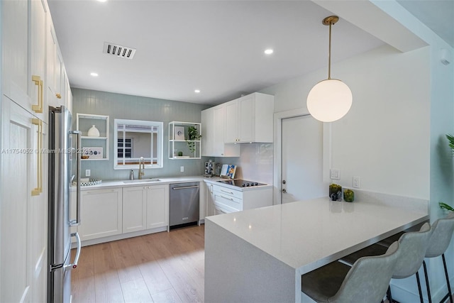 kitchen featuring visible vents, a peninsula, appliances with stainless steel finishes, a sink, and open shelves