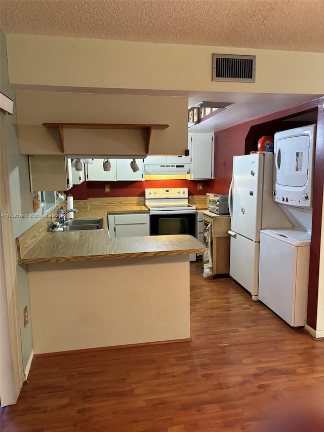 kitchen featuring under cabinet range hood, white appliances, a sink, visible vents, and stacked washing maching and dryer