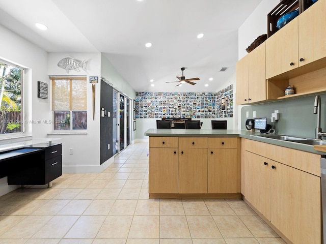 kitchen featuring a peninsula, backsplash, a sink, and light brown cabinetry