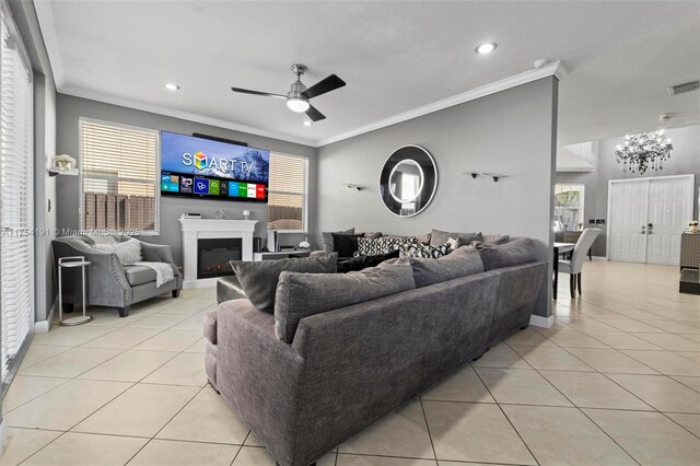 living area with light tile patterned floors, a warm lit fireplace, baseboards, ceiling fan, and ornamental molding