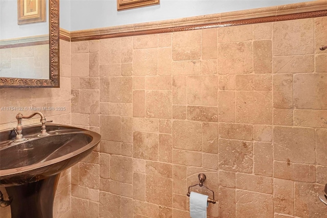 bathroom with a wainscoted wall, a sink, and tile walls