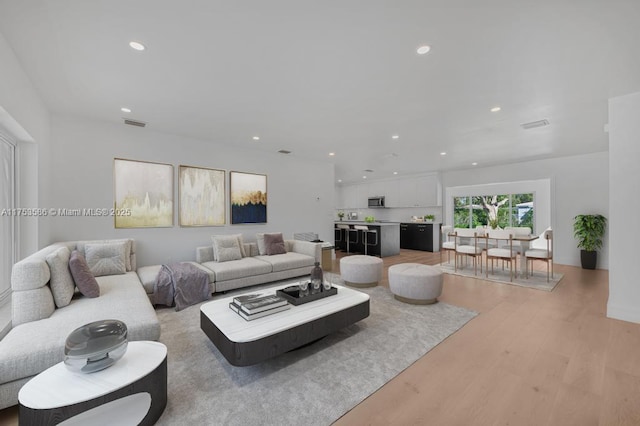 living area with light wood finished floors, visible vents, and recessed lighting