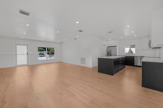 kitchen with light wood-style flooring, dark cabinets, stainless steel appliances, visible vents, and a center island