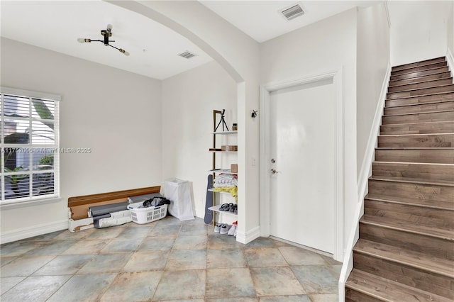 foyer entrance with arched walkways, visible vents, baseboards, and stairs