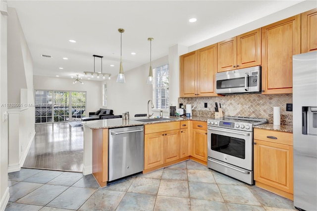 kitchen with tasteful backsplash, appliances with stainless steel finishes, a peninsula, light stone countertops, and a sink