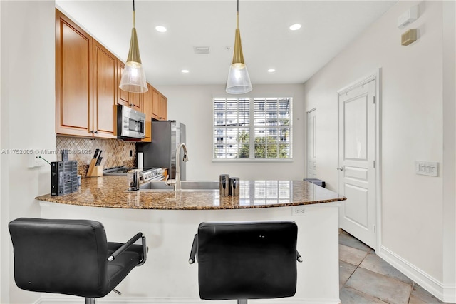 kitchen with stone counters, stainless steel appliances, decorative backsplash, a sink, and a peninsula