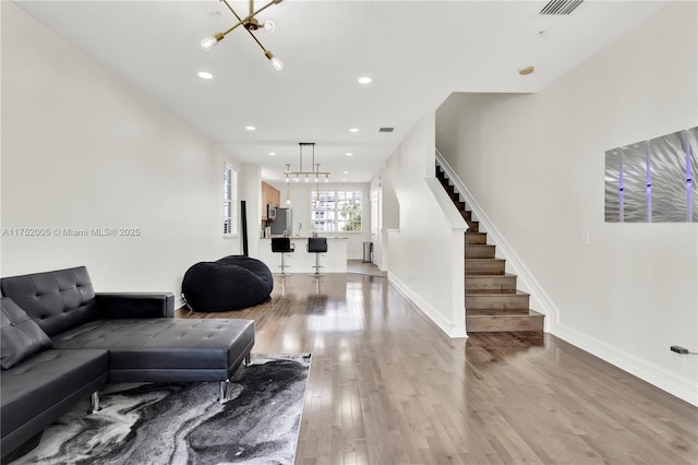 living area featuring recessed lighting, baseboards, light wood-style floors, stairway, and an inviting chandelier