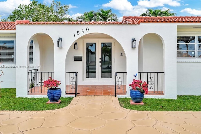 property entrance with stucco siding, a tiled roof, and french doors