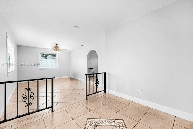 spare room featuring a ceiling fan, arched walkways, light tile patterned flooring, and baseboards