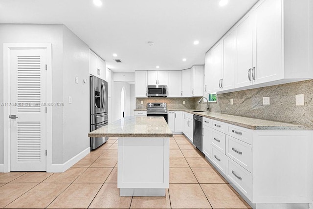 kitchen with light tile patterned floors, light stone counters, appliances with stainless steel finishes, a sink, and backsplash