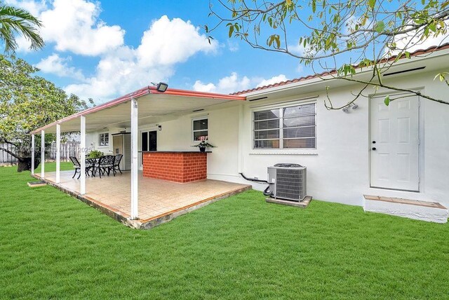 back of property with central AC, a tile roof, a yard, stucco siding, and a patio area