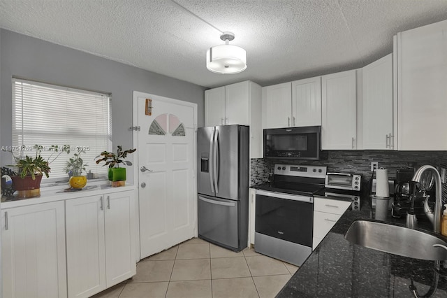 kitchen with light tile patterned floors, backsplash, appliances with stainless steel finishes, white cabinets, and a sink