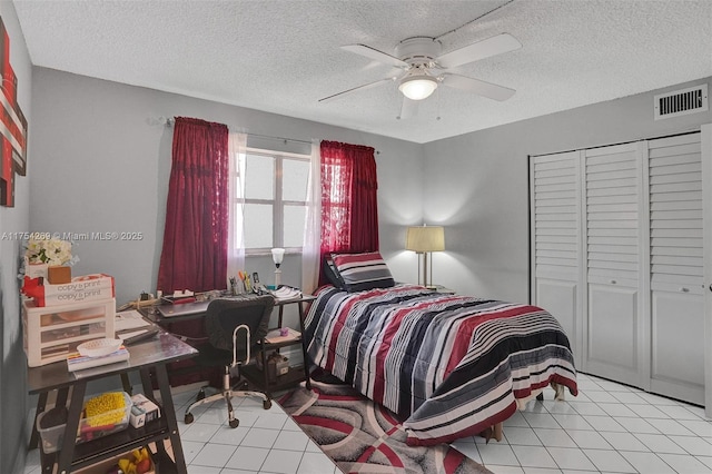 bedroom with light tile patterned floors, visible vents, ceiling fan, a textured ceiling, and a closet