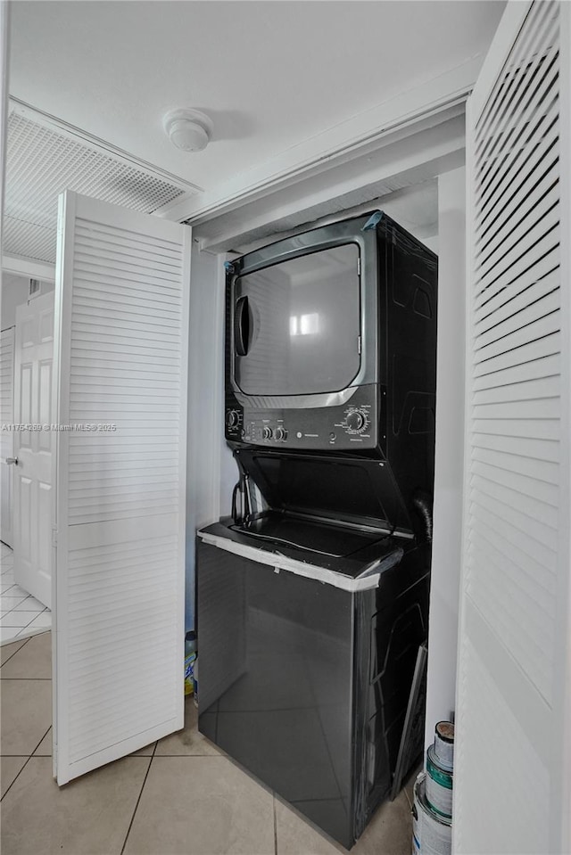 clothes washing area with tile patterned flooring, laundry area, and stacked washing maching and dryer