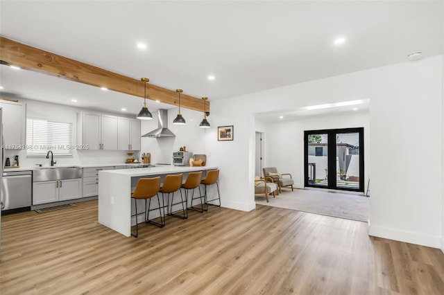 kitchen featuring a breakfast bar, light countertops, a sink, wall chimney range hood, and dishwasher