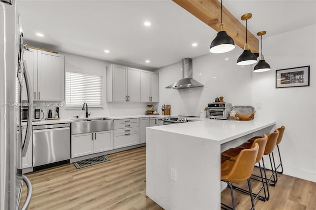 kitchen with wall chimney exhaust hood, a kitchen breakfast bar, a peninsula, stainless steel appliances, and a sink