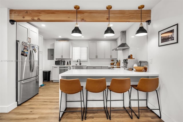 kitchen featuring appliances with stainless steel finishes, a sink, wall chimney range hood, a peninsula, and a kitchen breakfast bar