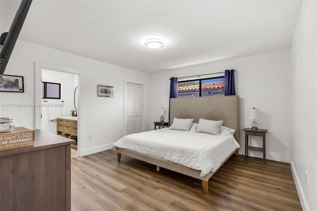 bedroom with a closet, ensuite bath, light wood-style flooring, and baseboards