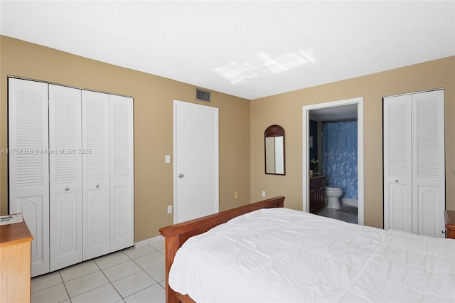 bedroom with multiple closets, visible vents, ensuite bath, and light tile patterned floors