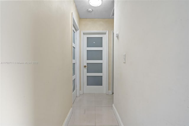 hall with light tile patterned floors, baseboards, and a textured ceiling