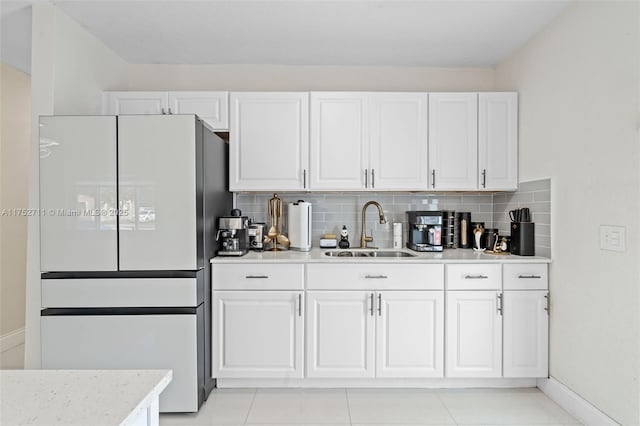 kitchen featuring light countertops, backsplash, freestanding refrigerator, white cabinets, and a sink